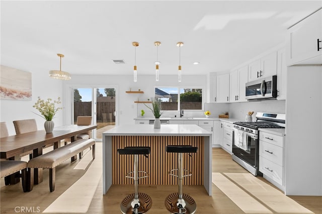 kitchen with decorative light fixtures, a kitchen island, a breakfast bar, appliances with stainless steel finishes, and white cabinets