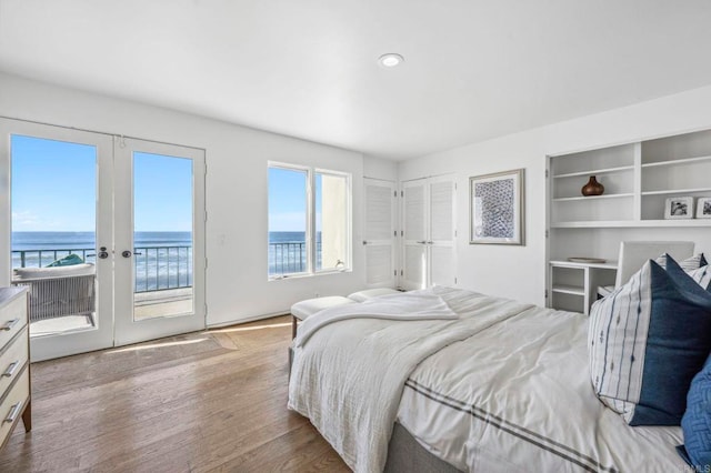 bedroom featuring french doors, access to exterior, a closet, a water view, and light hardwood / wood-style flooring