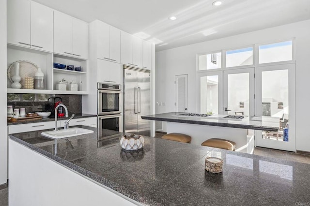 kitchen with sink, white cabinetry, a breakfast bar area, stainless steel appliances, and dark stone counters