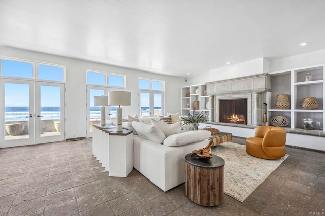 living room with a tiled fireplace, french doors, and a water view