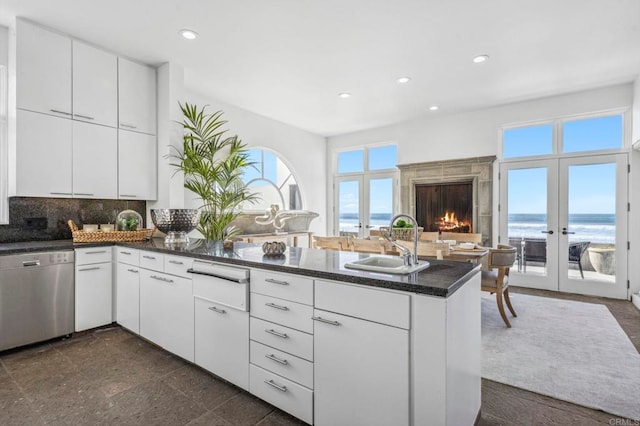 kitchen featuring stainless steel dishwasher, kitchen peninsula, sink, a water view, and white cabinets