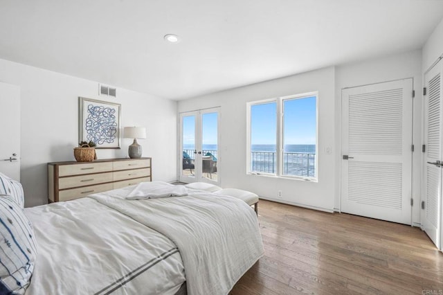 bedroom with dark wood-type flooring, a water view, and french doors