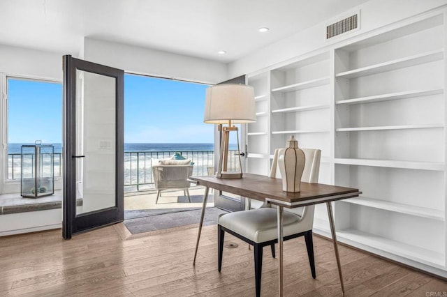 office space featuring a water view, built in features, a beach view, and hardwood / wood-style flooring