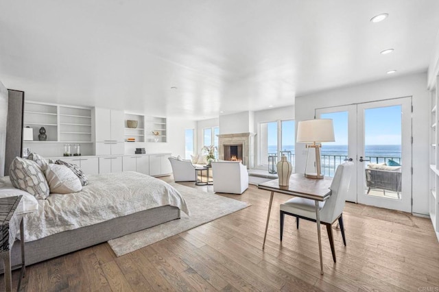 bedroom featuring a water view, access to exterior, french doors, and light hardwood / wood-style floors