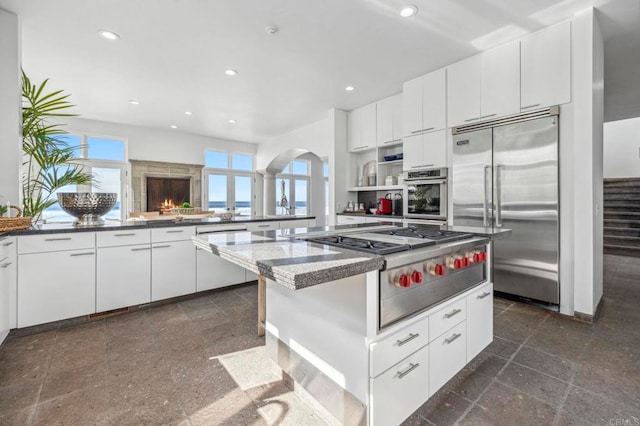 kitchen with appliances with stainless steel finishes, dark stone countertops, a kitchen island, white cabinets, and a breakfast bar