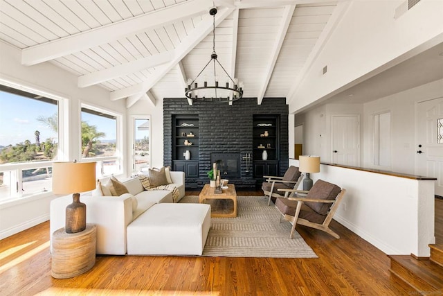 sitting room featuring hardwood / wood-style flooring, a brick fireplace, built in features, a chandelier, and lofted ceiling with beams