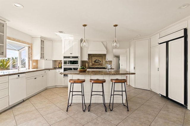 kitchen featuring stainless steel double oven, a kitchen island, dark stone counters, tasteful backsplash, and white dishwasher