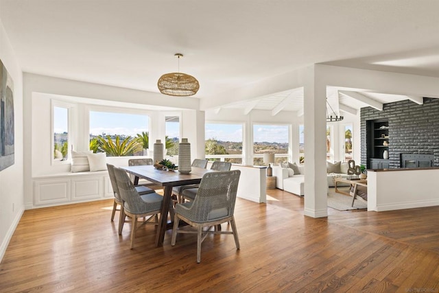 dining area featuring built in shelves, a large fireplace, beamed ceiling, and hardwood / wood-style flooring