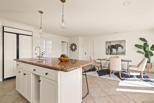 kitchen featuring white cabinetry, dark stone counters, paneled built in refrigerator, sink, and a kitchen island with sink