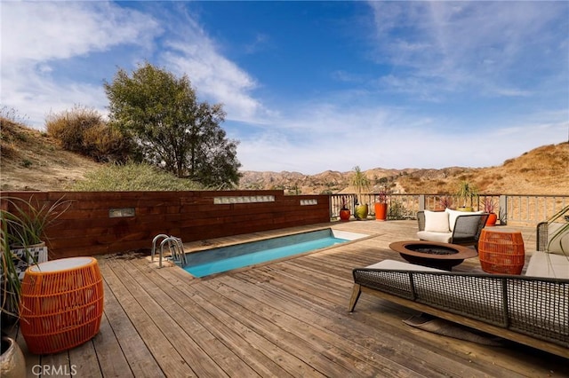 view of swimming pool featuring a deck with mountain view and an outdoor living space with a fire pit