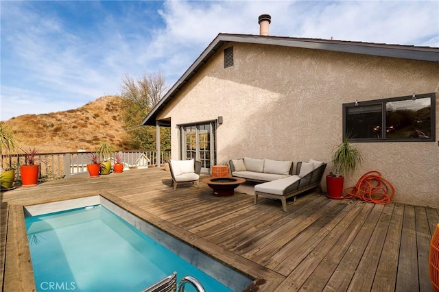 back of property with a deck with mountain view and an outdoor living space with a fire pit