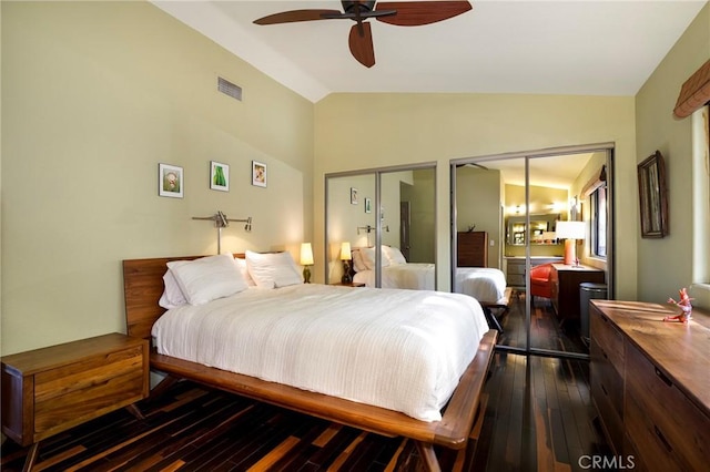 bedroom with ceiling fan, dark wood-type flooring, two closets, and vaulted ceiling