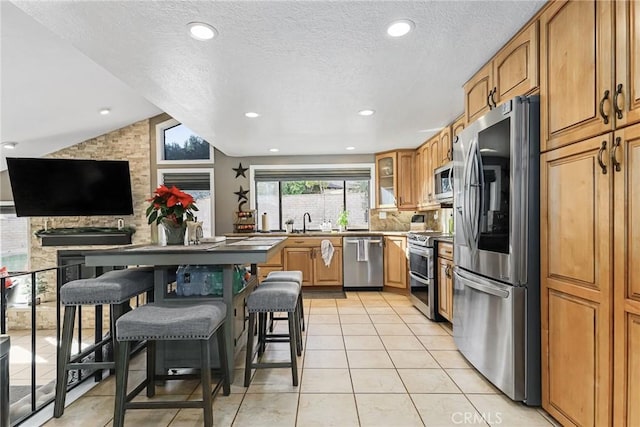 kitchen with lofted ceiling, a kitchen bar, sink, appliances with stainless steel finishes, and light tile patterned floors