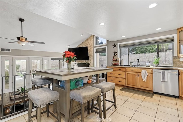 kitchen with light tile patterned floors, a breakfast bar area, vaulted ceiling, stainless steel dishwasher, and sink