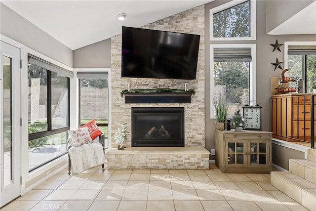 living room featuring vaulted ceiling, light tile patterned floors, and a stone fireplace