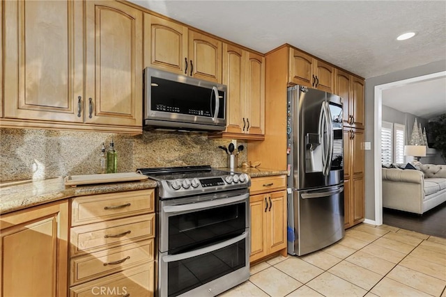 kitchen with light tile patterned floors, appliances with stainless steel finishes, decorative backsplash, and light stone countertops