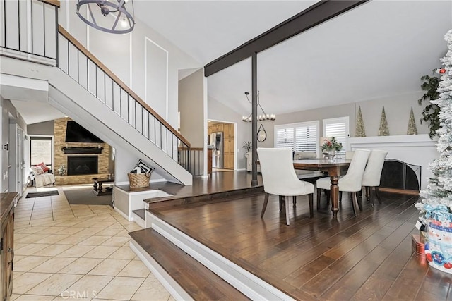 dining space featuring light tile patterned floors, vaulted ceiling, an inviting chandelier, and a stone fireplace