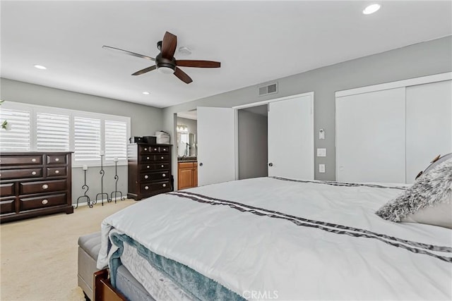 bedroom with ceiling fan, light colored carpet, and ensuite bathroom