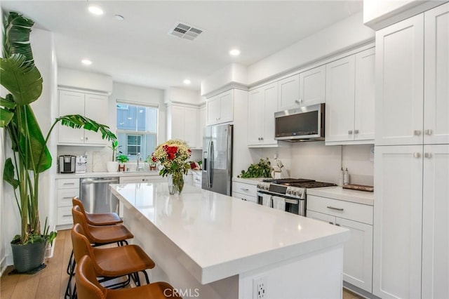 kitchen with appliances with stainless steel finishes, a kitchen bar, white cabinets, and a center island