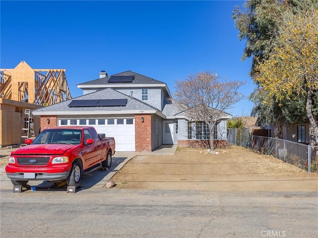 traditional-style house featuring brick siding, solar panels, an attached garage, fence, and driveway