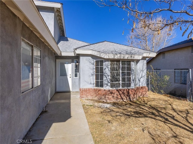 doorway to property featuring roof with shingles, fence, brick siding, and stucco siding