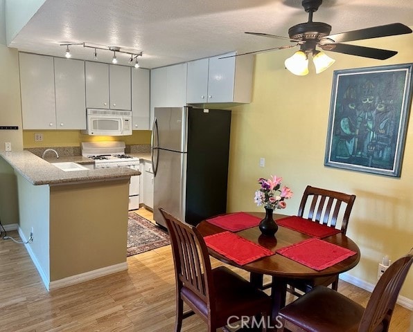 kitchen with white cabinetry, kitchen peninsula, ceiling fan, white appliances, and sink