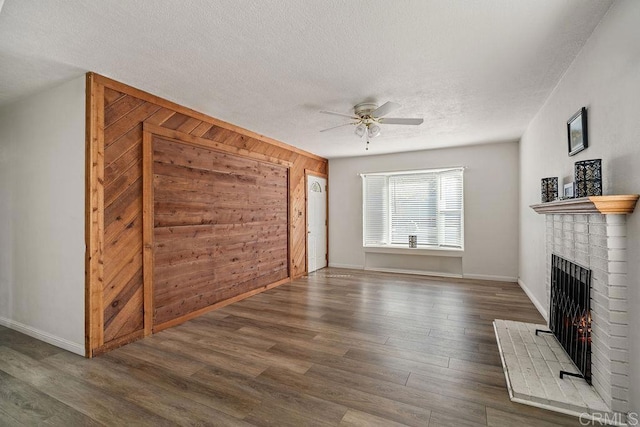 unfurnished living room with a brick fireplace, a textured ceiling, ceiling fan, dark hardwood / wood-style floors, and wood walls