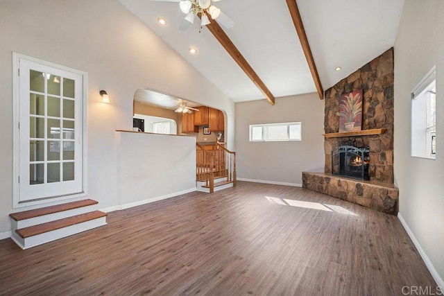 unfurnished living room featuring beam ceiling, high vaulted ceiling, ceiling fan, and a stone fireplace