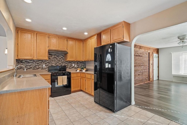 kitchen featuring ceiling fan, sink, wood walls, light tile patterned floors, and black appliances