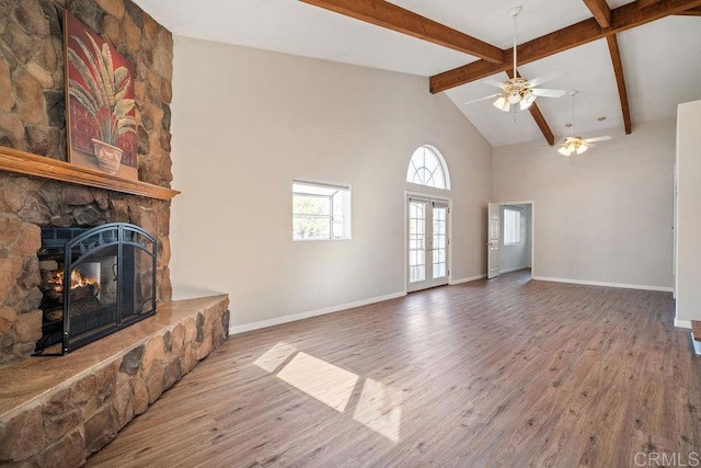 unfurnished living room featuring ceiling fan, french doors, beamed ceiling, a fireplace, and hardwood / wood-style flooring