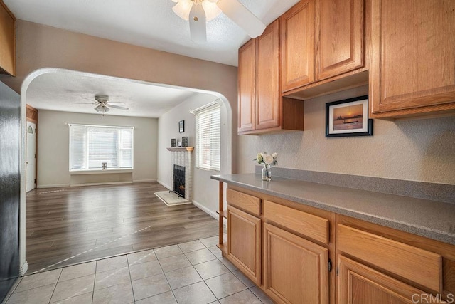 kitchen featuring ceiling fan, light tile patterned floors, and a brick fireplace