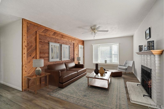 living room featuring wood walls, a brick fireplace, ceiling fan, a textured ceiling, and dark hardwood / wood-style flooring