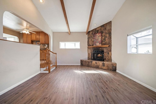 unfurnished living room with ceiling fan, lofted ceiling with beams, a stone fireplace, and dark hardwood / wood-style floors