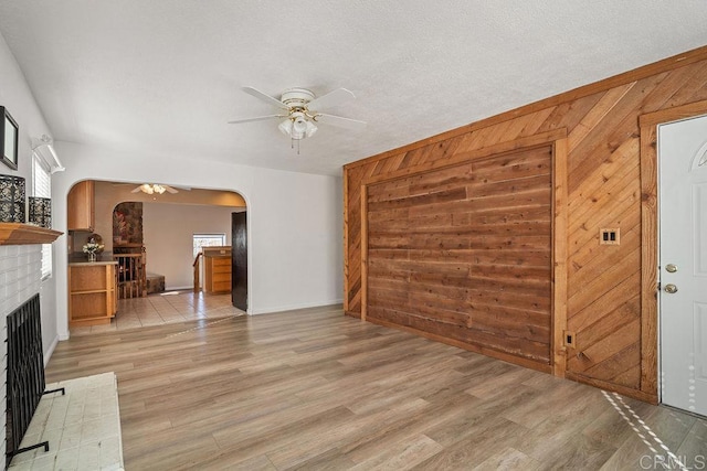 unfurnished living room with wood walls, light hardwood / wood-style flooring, ceiling fan, a textured ceiling, and a fireplace