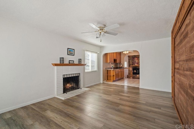 unfurnished living room with hardwood / wood-style flooring, ceiling fan, a textured ceiling, and a brick fireplace