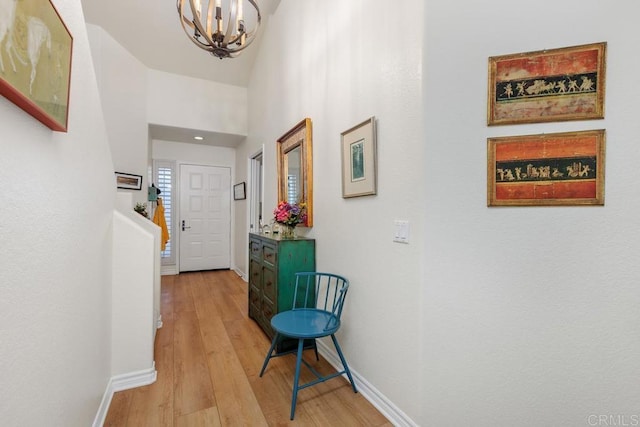 hall with a towering ceiling, an inviting chandelier, and light hardwood / wood-style floors