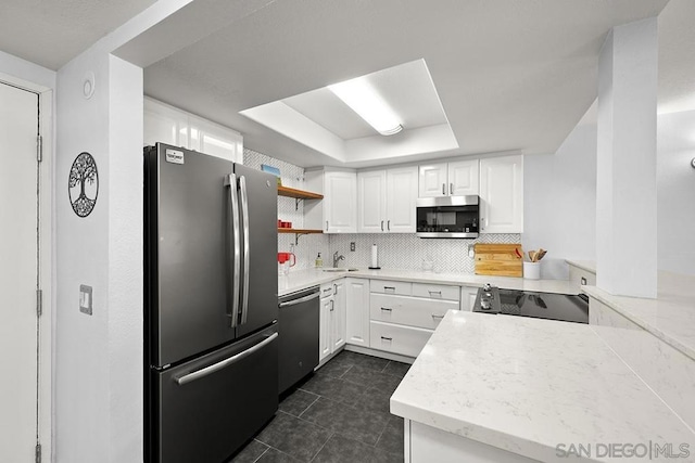 kitchen featuring white cabinetry, appliances with stainless steel finishes, decorative backsplash, a tray ceiling, and sink