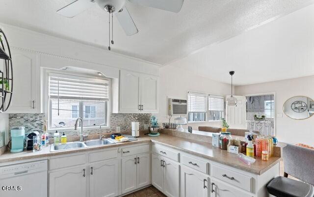 kitchen with a wall mounted AC, dishwasher, hanging light fixtures, white cabinets, and sink