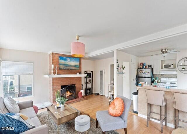 living room with light wood-type flooring, a brick fireplace, and ceiling fan