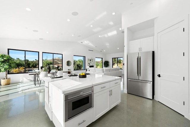 kitchen with light stone countertops, white cabinetry, a kitchen island, and stainless steel refrigerator