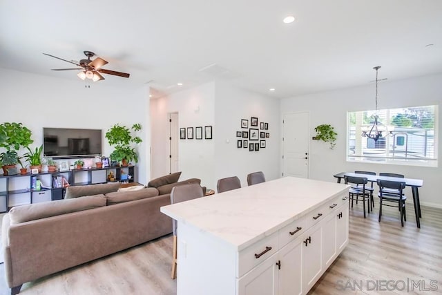 kitchen with decorative light fixtures, a kitchen island, a breakfast bar area, white cabinets, and ceiling fan with notable chandelier