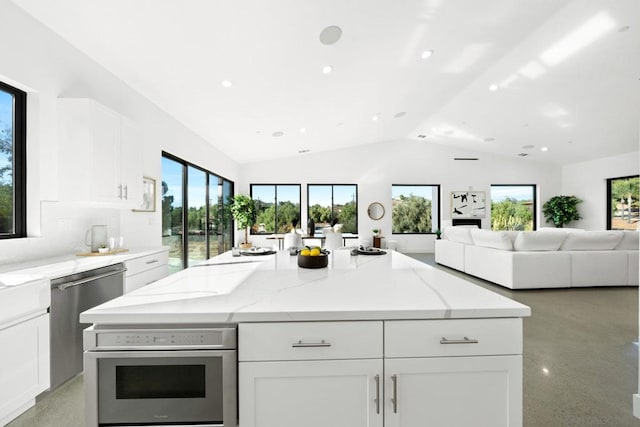 kitchen with light stone countertops, white cabinets, appliances with stainless steel finishes, a center island, and vaulted ceiling