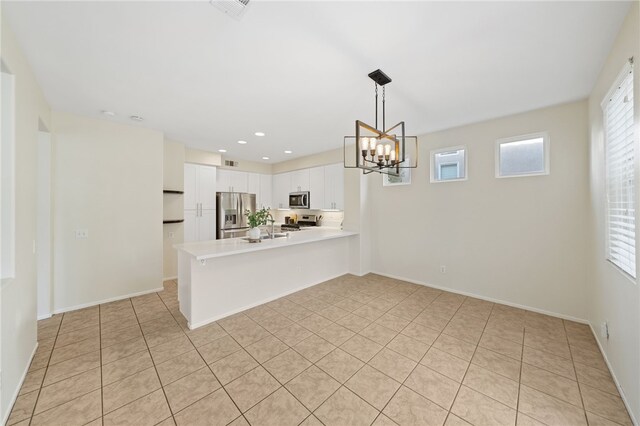 kitchen with light tile patterned flooring, appliances with stainless steel finishes, white cabinets, a notable chandelier, and kitchen peninsula