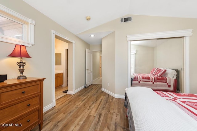 bedroom with vaulted ceiling, ensuite bathroom, a closet, and light wood-type flooring