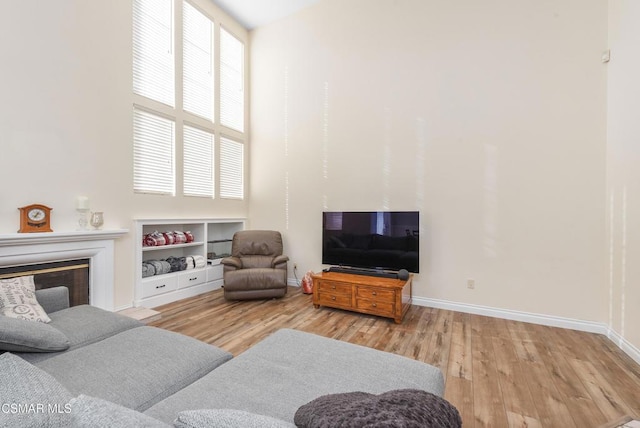 living room featuring a towering ceiling, built in features, and light hardwood / wood-style flooring