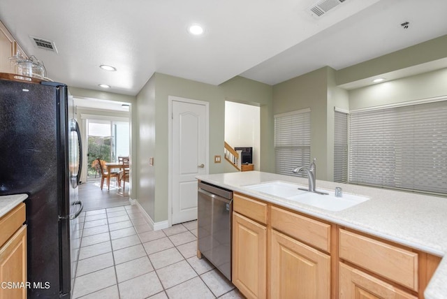 kitchen with stainless steel dishwasher, sink, black refrigerator, light tile patterned floors, and light brown cabinetry