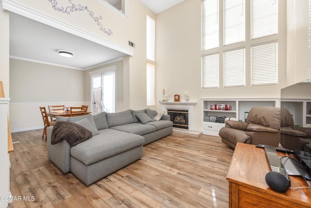 living room featuring built in shelves, a tile fireplace, crown molding, and light hardwood / wood-style flooring