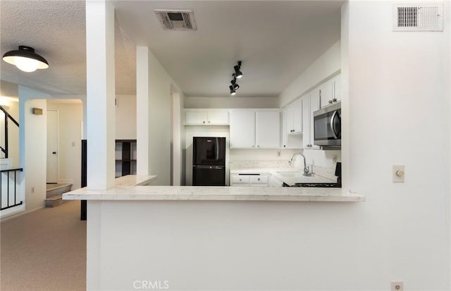 kitchen with stove, kitchen peninsula, sink, white cabinetry, and black refrigerator