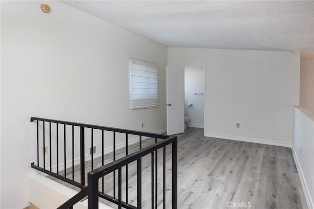 corridor with a textured ceiling and light hardwood / wood-style flooring