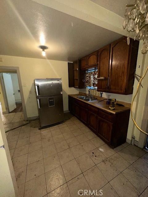 kitchen with stainless steel refrigerator with ice dispenser, sink, a textured ceiling, and dark brown cabinets